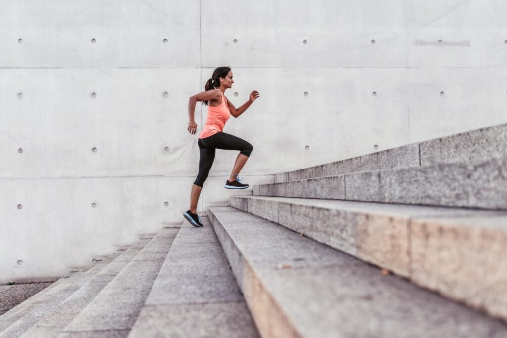 Woman running up outdoor stairs in athletic clothing for knee strength training