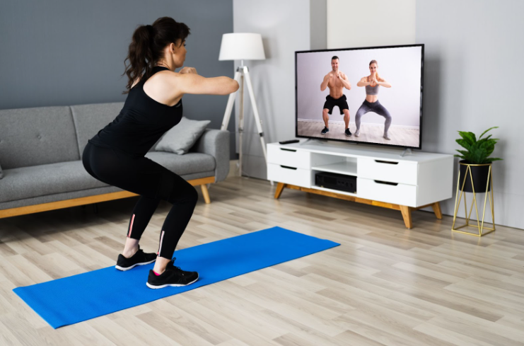 Woman doing squats at home while following online workout video on TV